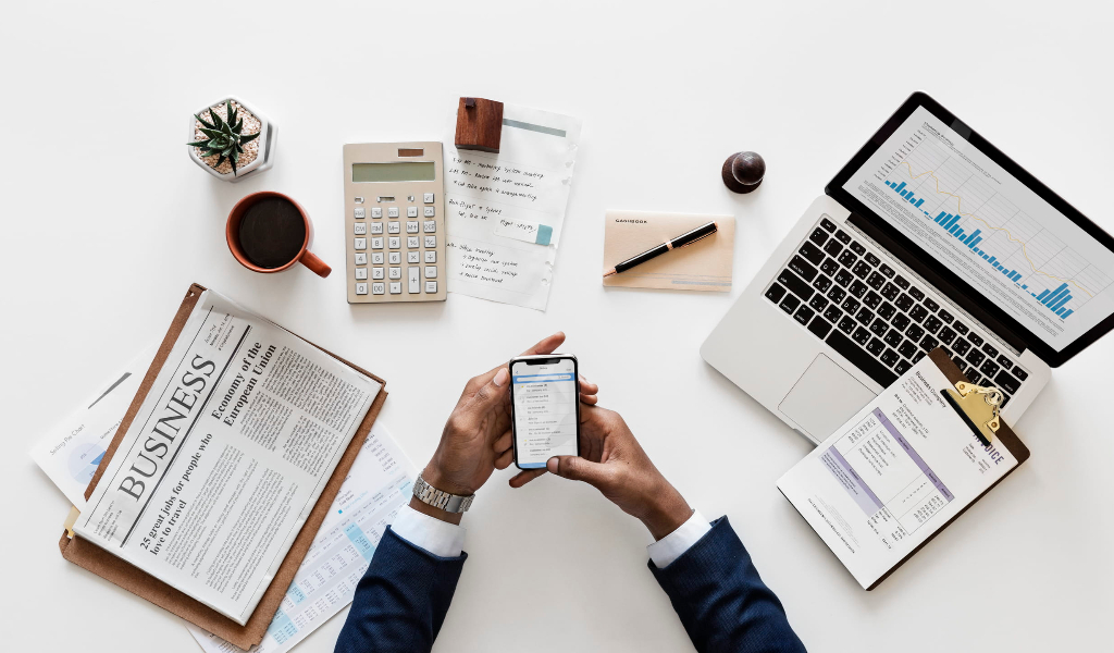 The Fintech & Blockchain Dictionary: What You Need to Know (And What They Won't Tell You). a man checking a smartphone with pc, neswpaper, and other things on the table