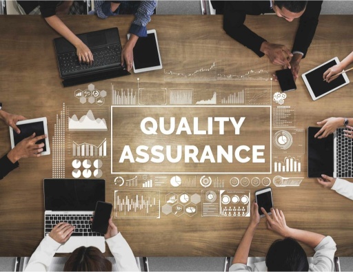 employees at a meeting with the word quality assurance appears on the table